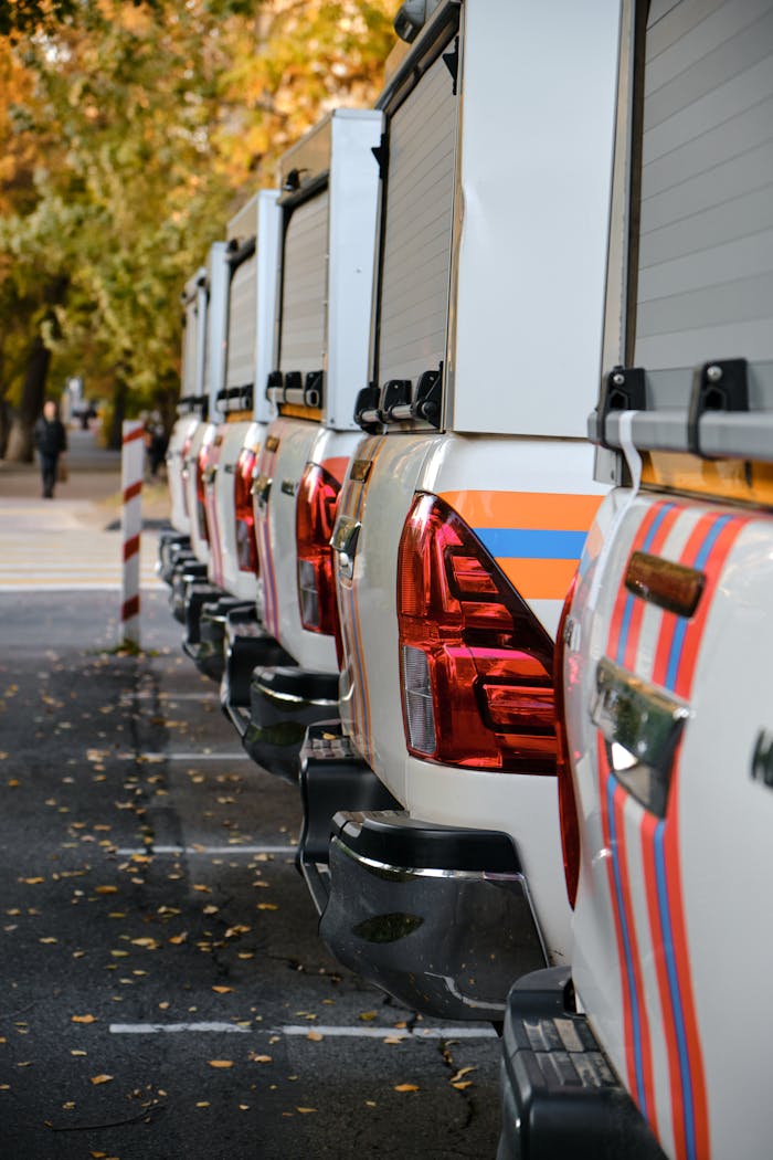 A row of pick-up trucks parked outdoors during autumn with falling leaves.
